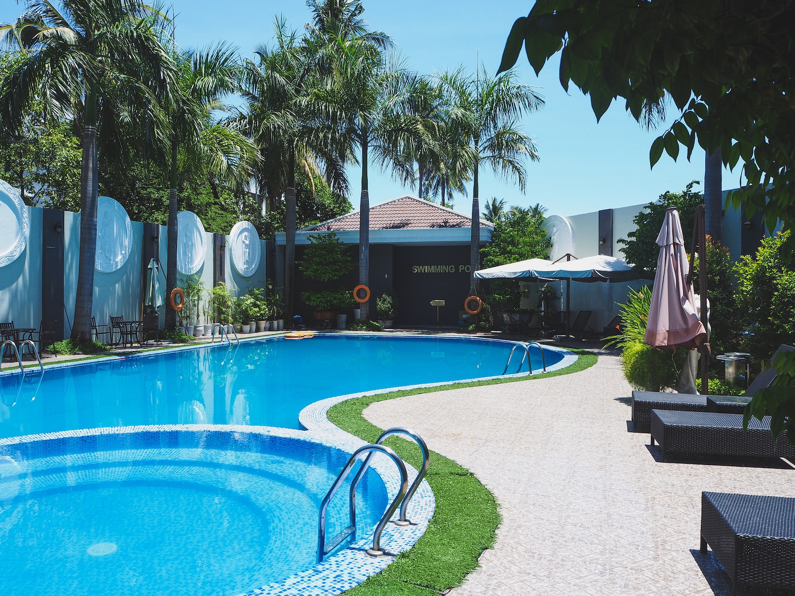 Piscina al aire libre con tumbonas en territorio de hotel tropical con palmeras verdes contra el cielo azul sin nubes