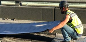 US 2 Paving: Worker laying down waterproof material